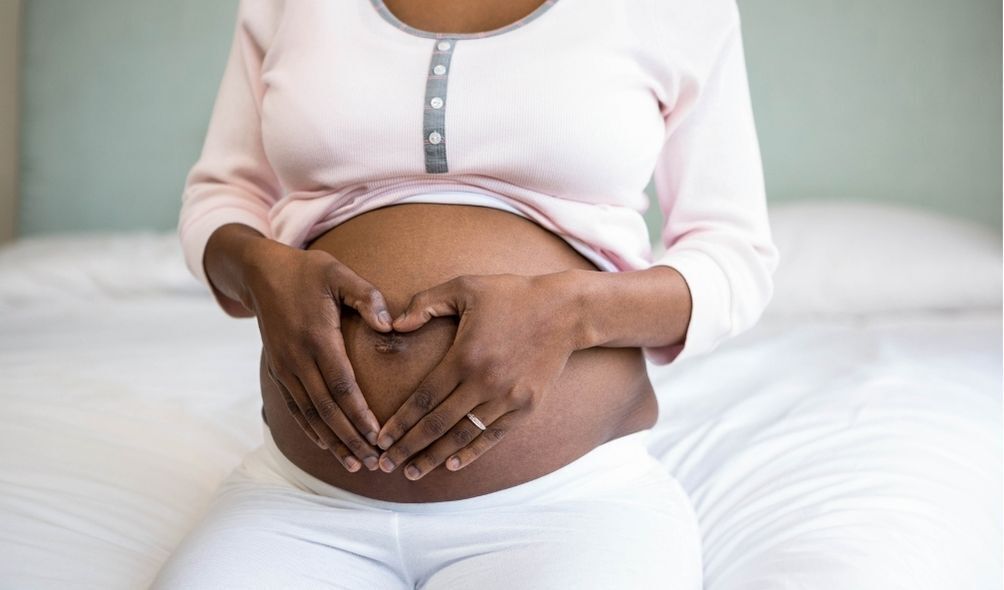 Mulher grávida fazendo coração no umbigo