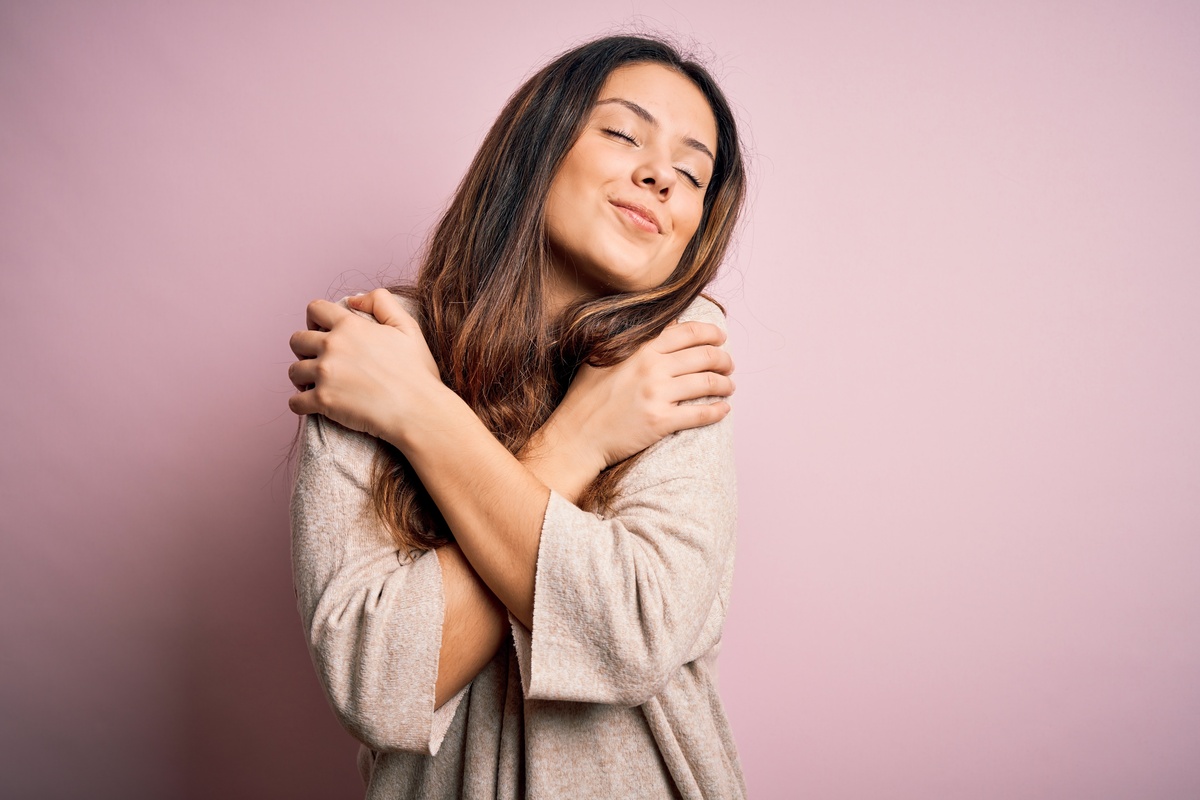 Mulher abraçando os próprios ombros, em sinal de amor próprio, que é praticado por meio do Ho'oponopono.