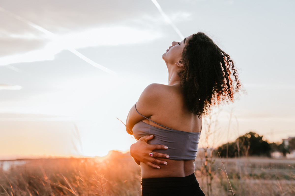 Mulher abraçando o próprio corpo enquanto se guia para o horizonte, em sinal de aceitação e amor próprio, duas das mensagens encontradas na filosofia Ho'oponopono. 