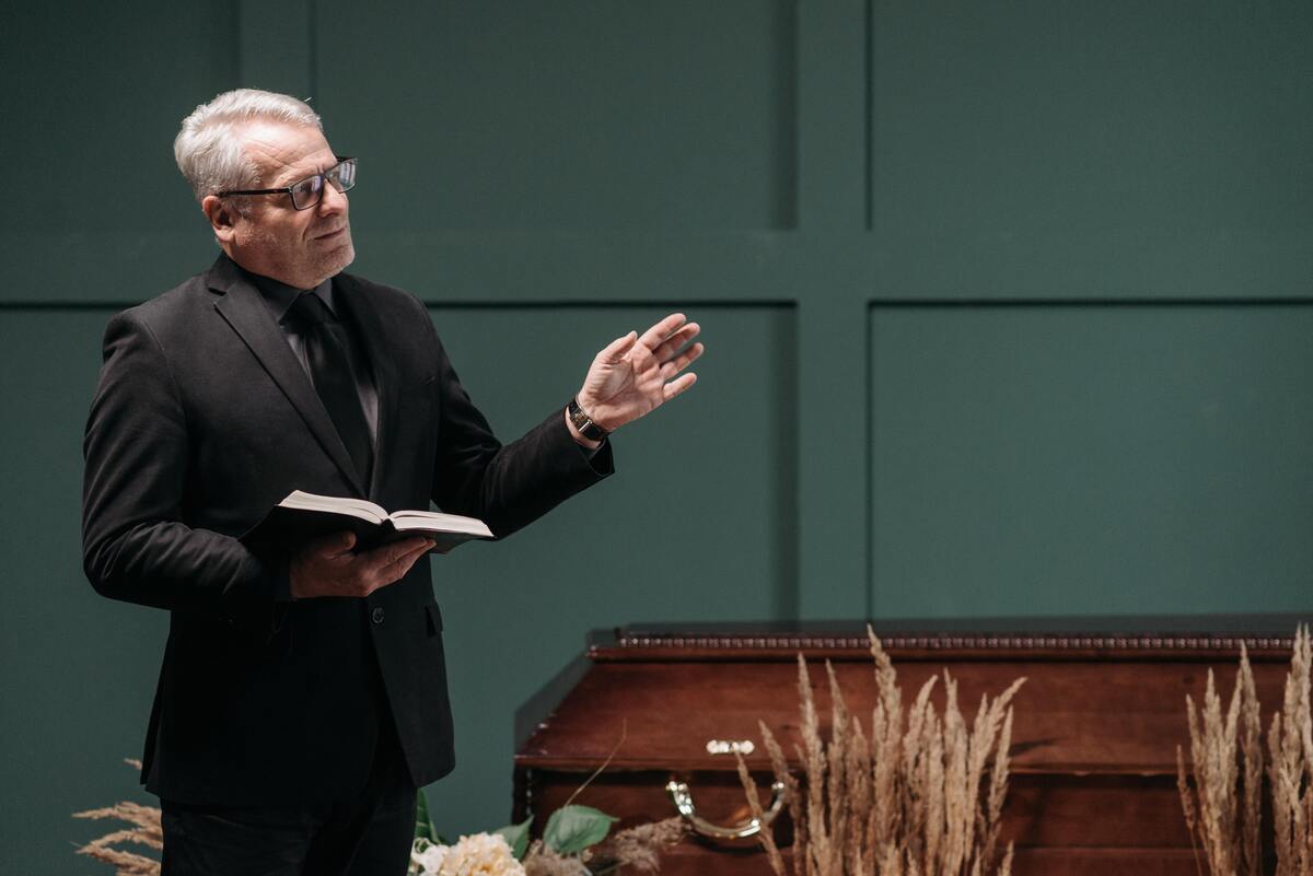 Padre falando ao lado de um caixão.