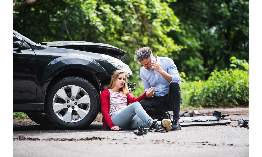 Homem ajudando uma mulher sentada no chão após um acidente de carro.