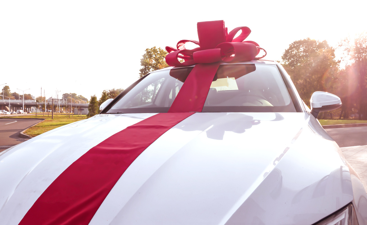 Carro novo branco estacionado com laço vermelho.