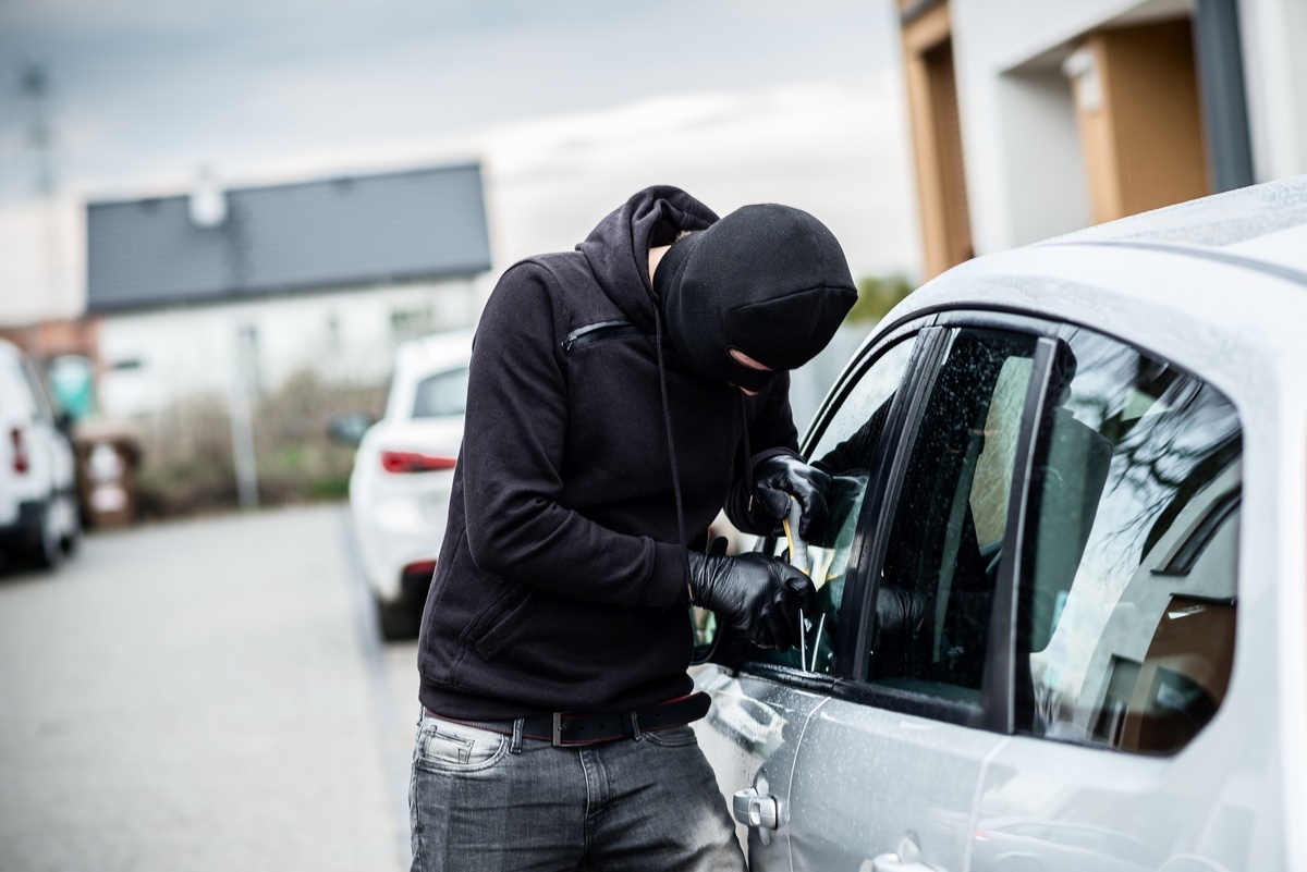 Homem tentando abrir janela de carro para roubá-lo.