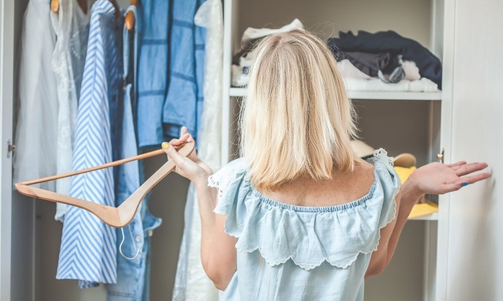 Mulher encarando guarda-roupa aberto.