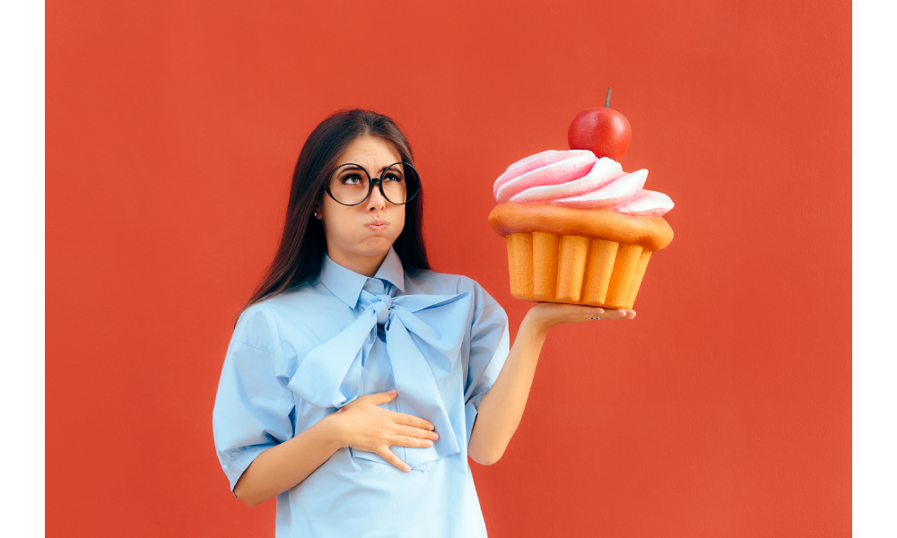 Mulher que comeu demais segurando um objeto em formato de cupcake.