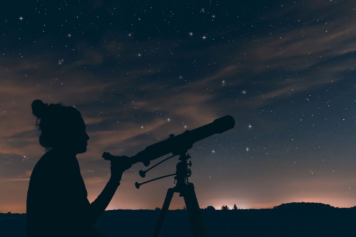 Mulher observando astros no céu com luneta.