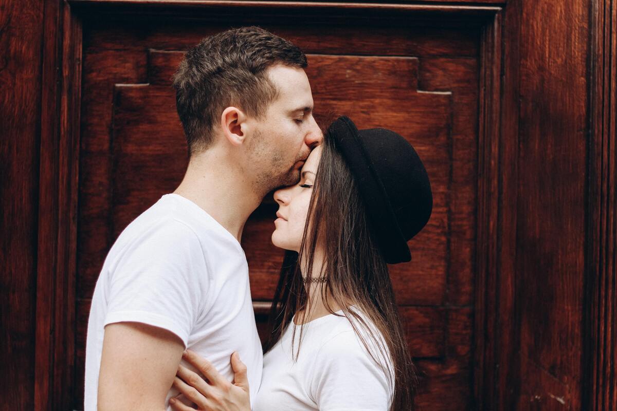 Homem beijando testa de uma mulher.