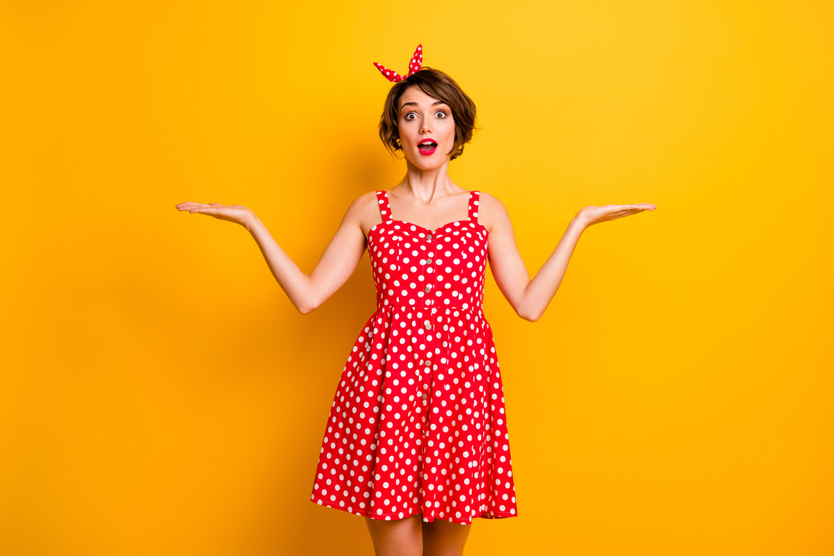 Mulher posando em fundo amarelo, enquanto veste um vestido vermelho e branco.