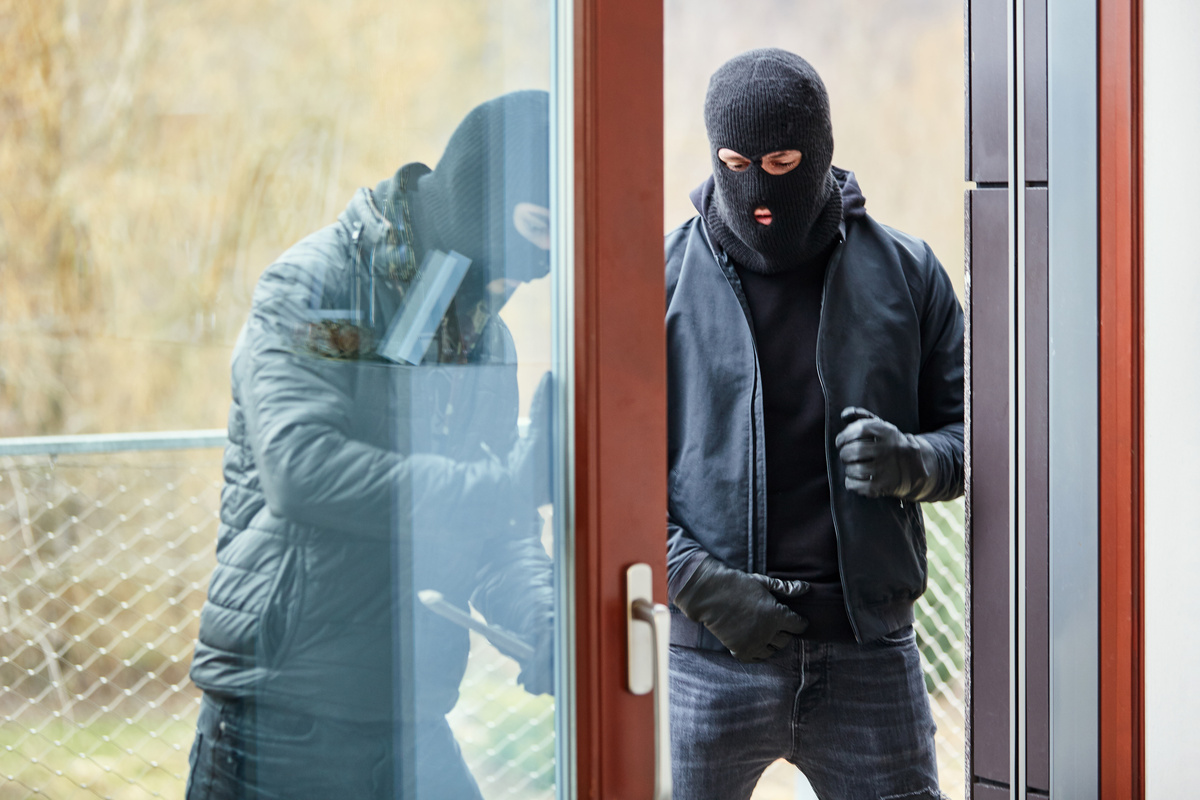 Dois homens tentando arrombar porta de casa para invadir.