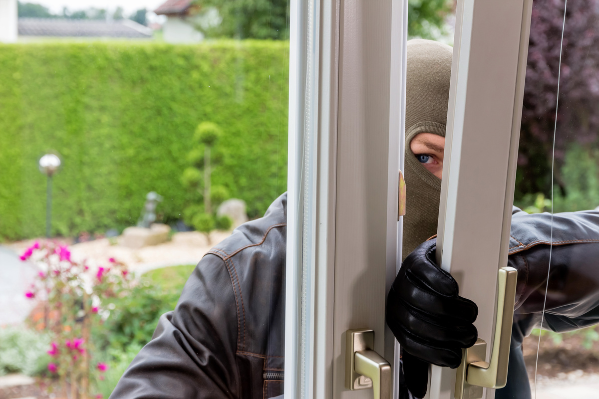 Homem invadindo casa pela porta de vidro do jardim.