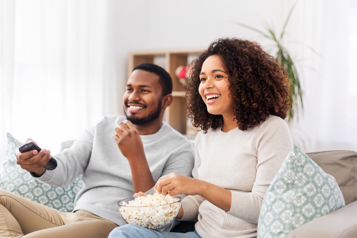 Casal de Libra e Sagitário se divertindo vendo TV e comendo pipoca.