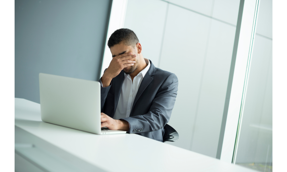 Homem preocupado sentado em uma mesa com um notebook.