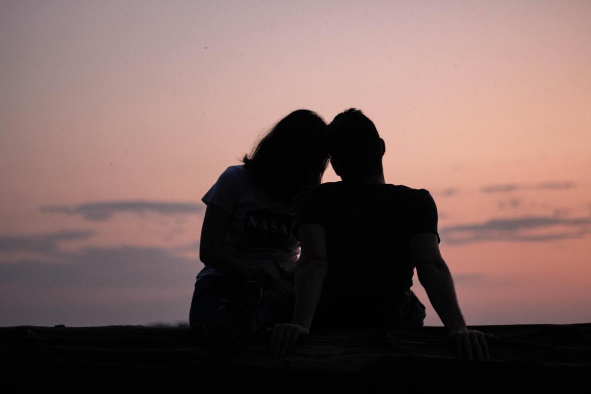 Silhueta de um casal abraçado olhando o por do sol. 