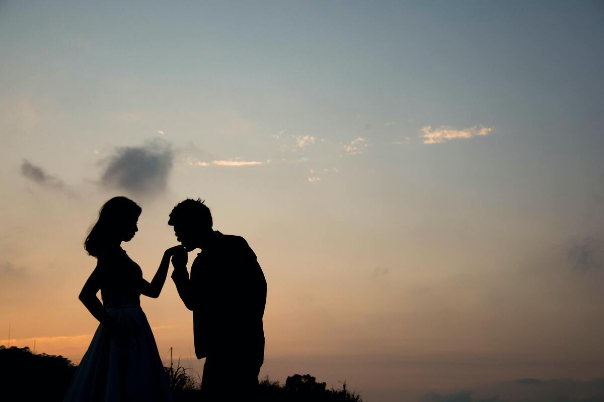 Silhueta de um homem beijando a mão de uma mulher.