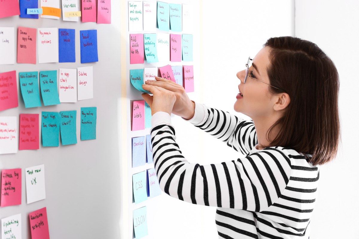 Pessoas do terceiro decanato de Capricórnio são organizadas. Imagem mostra mulher colocando post-its numa parede.