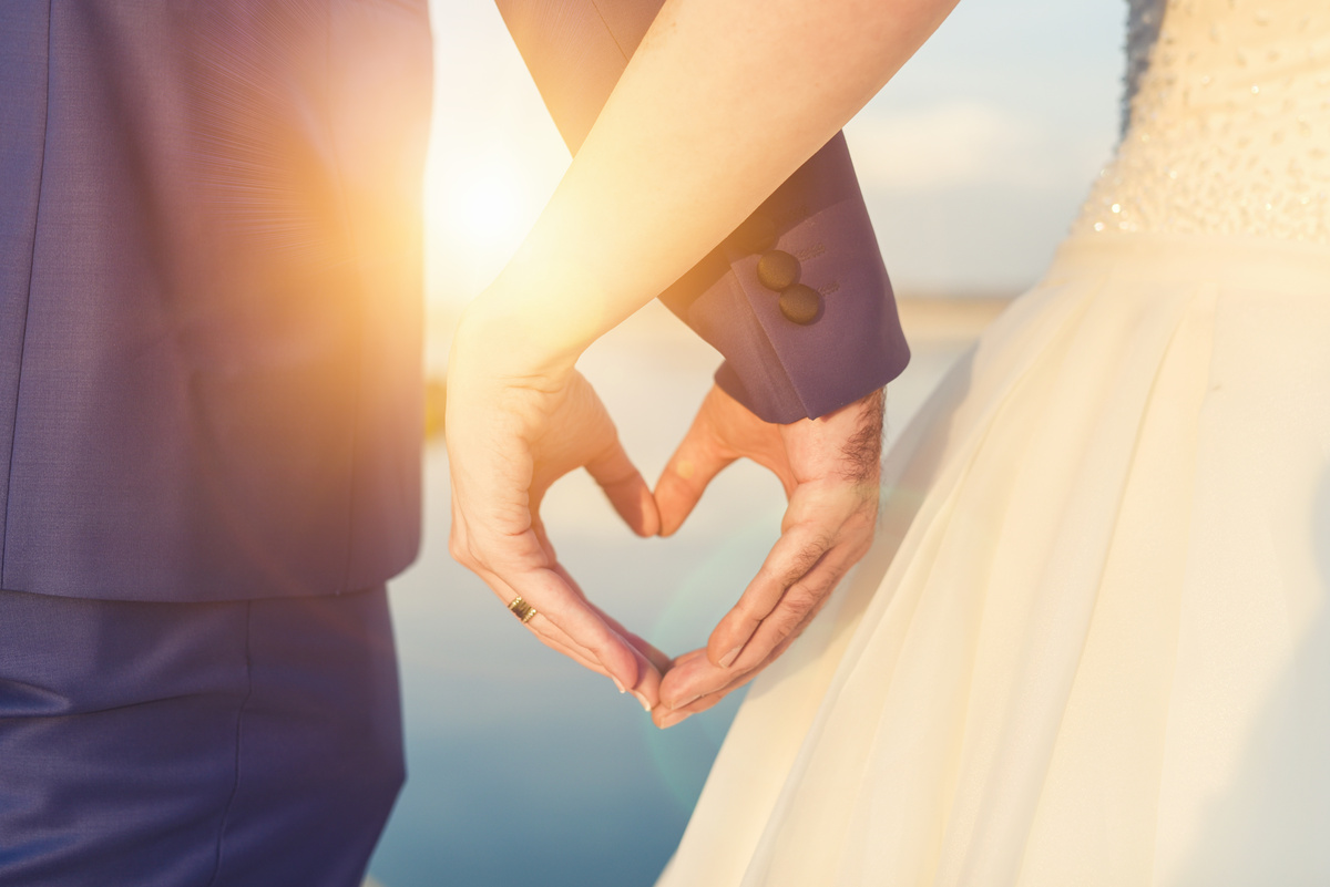 Casal lado a lado formando coração com as mãos