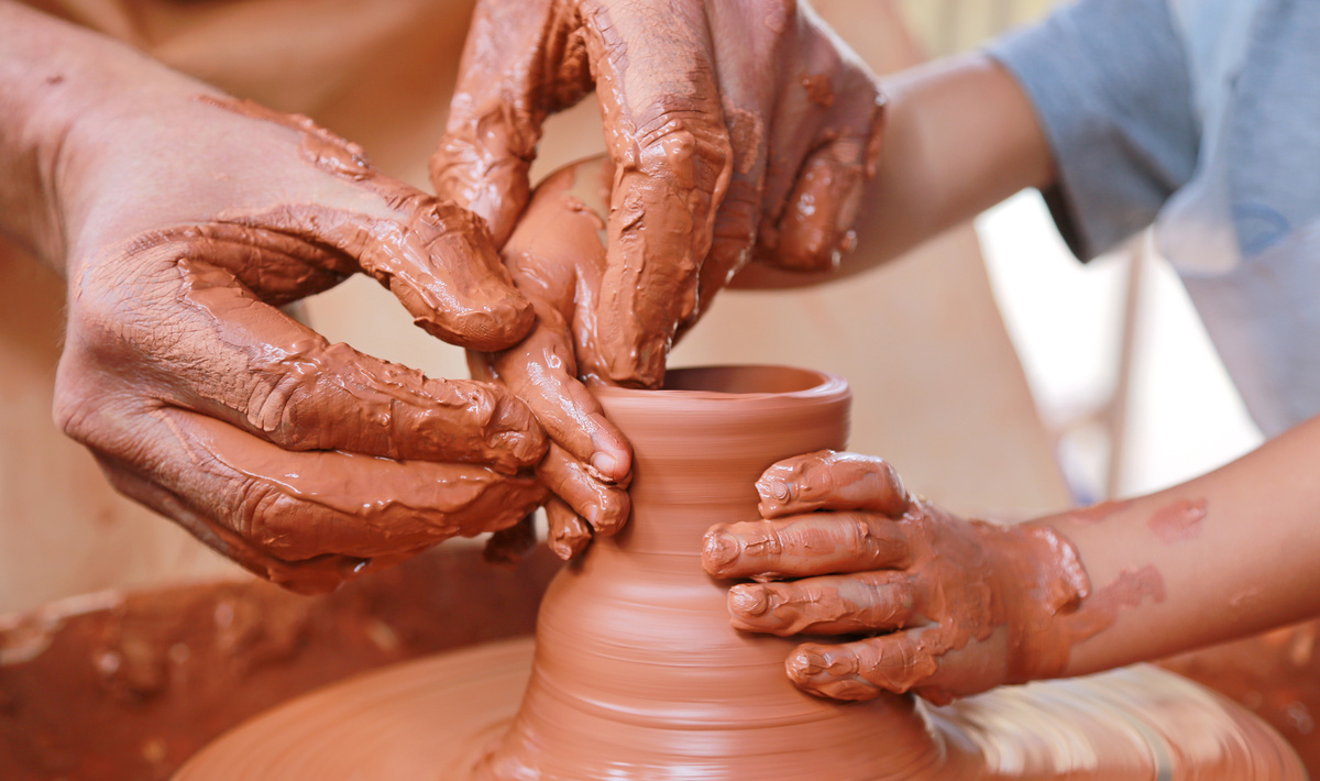 Adulto e criança moldando vaso de barro