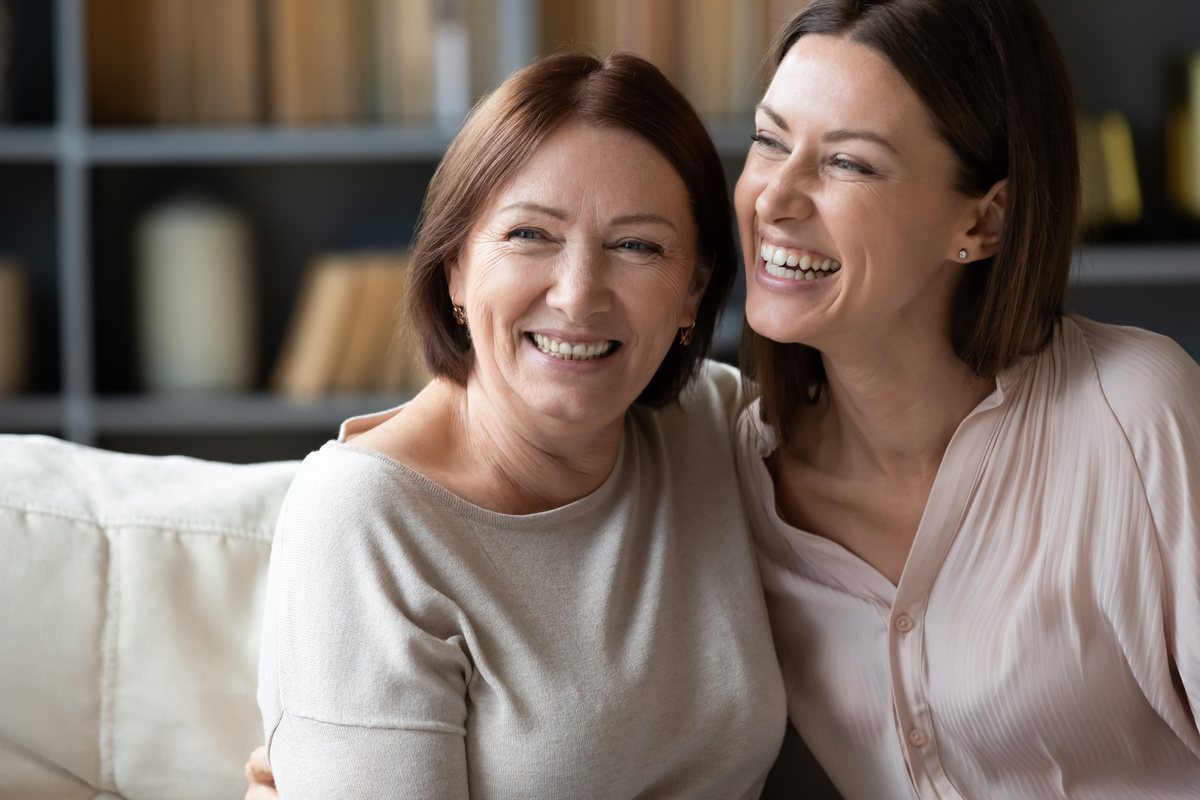 Mãe e filha abraçadas, sorrindo e sentadas em um sofá