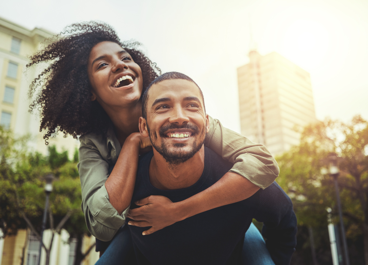 Casal se divertindo na cidade, com mulher nas costas do homem.