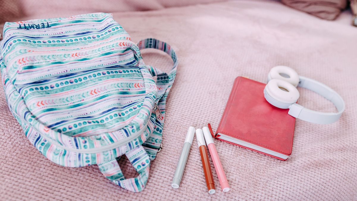 Mochila jogada na cama com caderno e fone de ouvido.