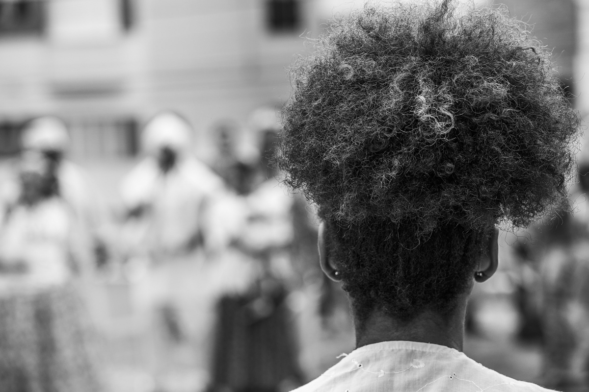 Mulher de costas, pessoas rezando em um culto da Umbanda ao fundo.