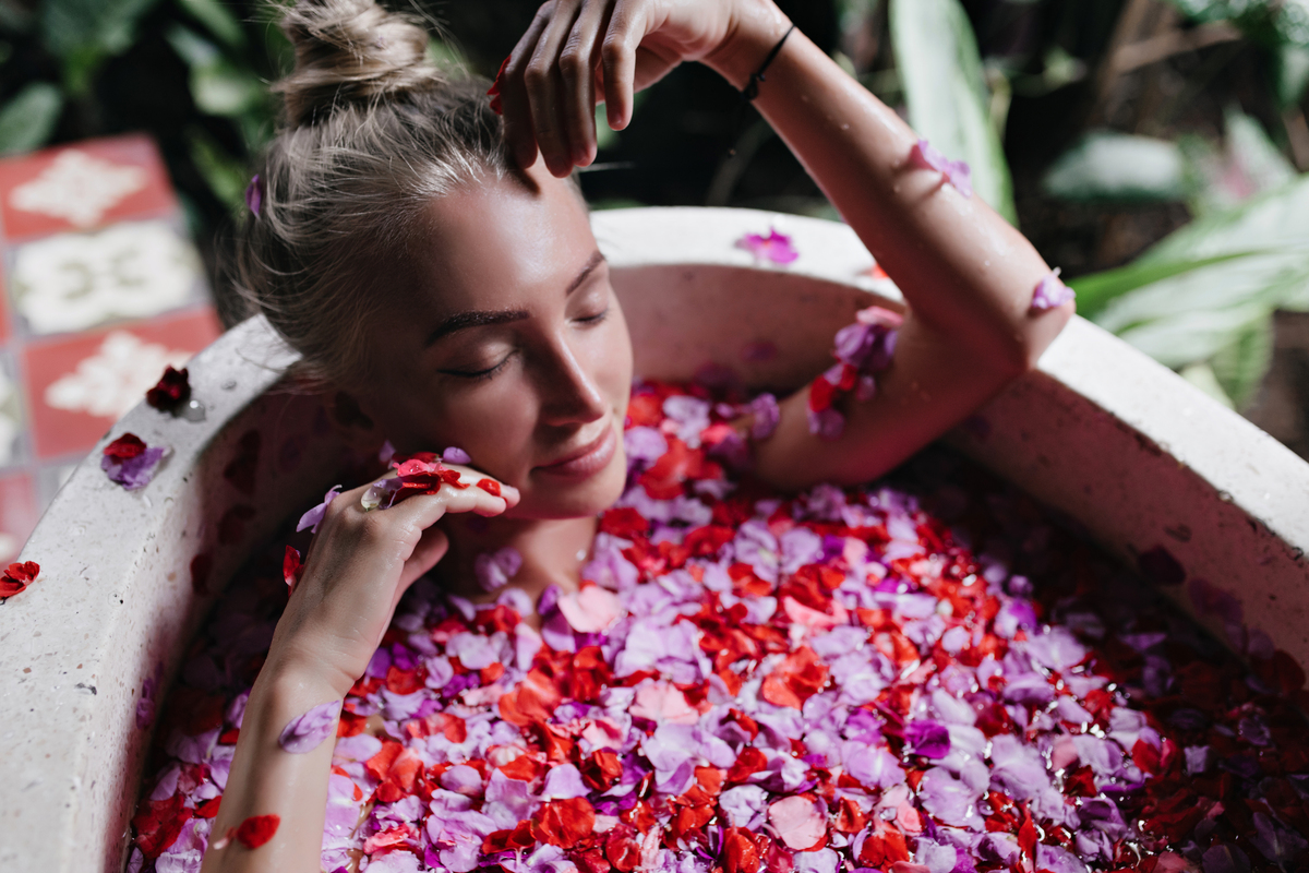 Mulher relaxando em banho de pétalas vermelhas e rosas