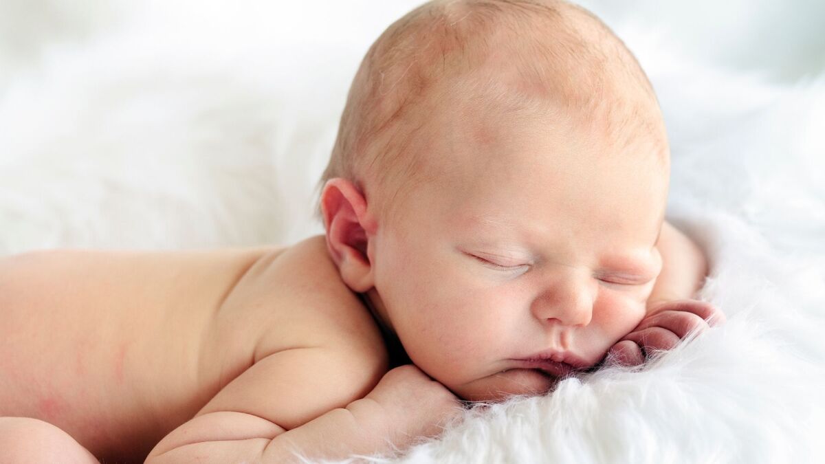 Bebê dormindo em um lençol branco.