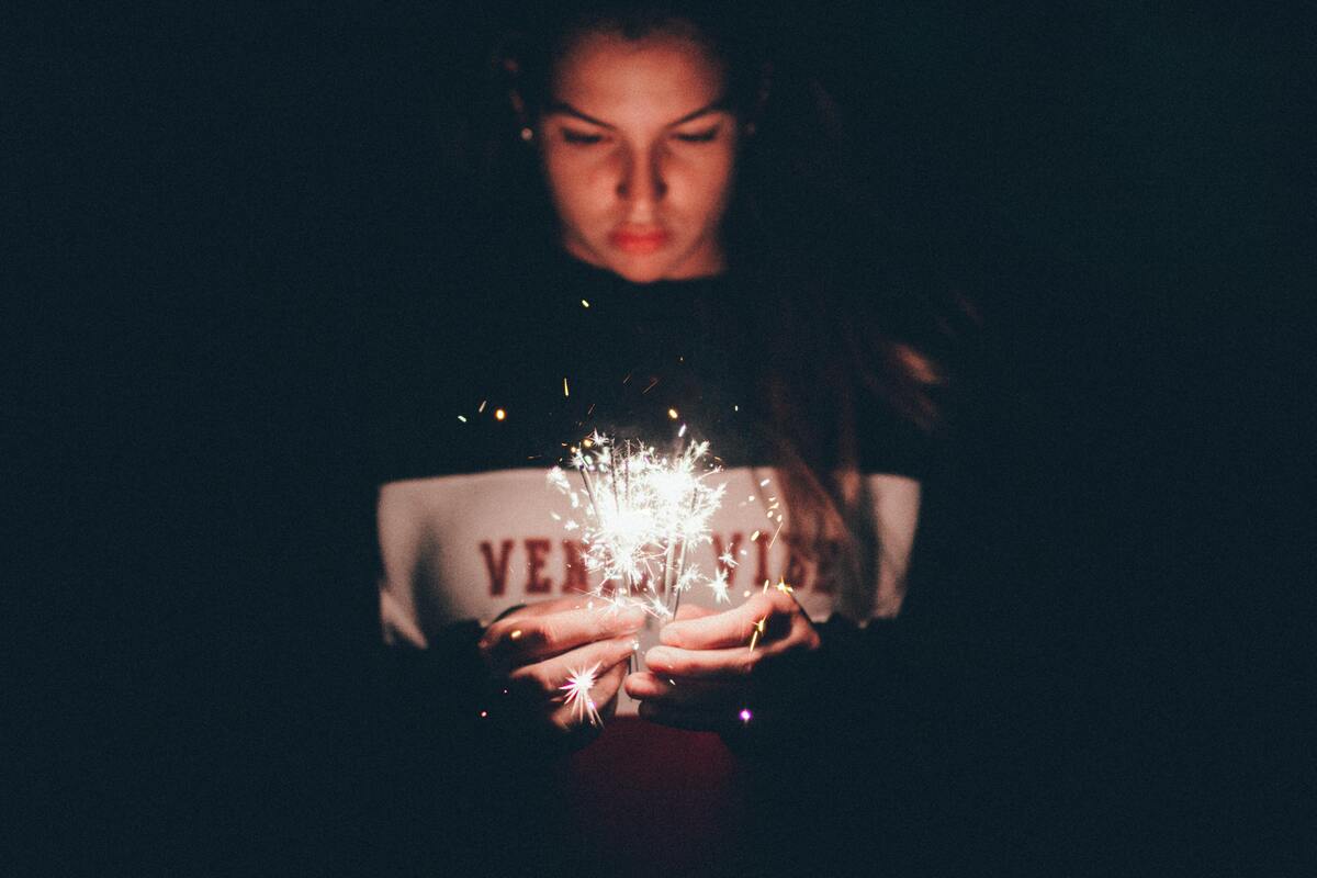 Menina usando blusa preta e branca, com diversas velas acesas. 