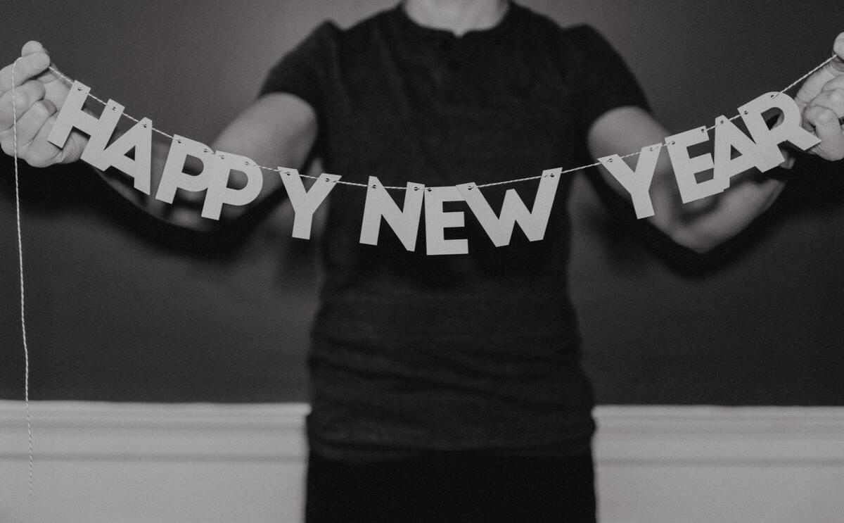 Homem vestido preto, segurando letras que escrevem "Feliz Ano Novo" em inglês. 