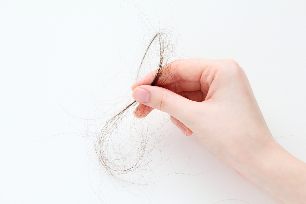 Mão segurando fio de cabelo.