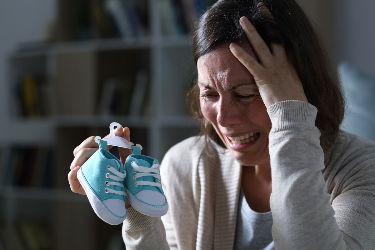 Mãe chorando com sapatinhos de bebê nas mãos.