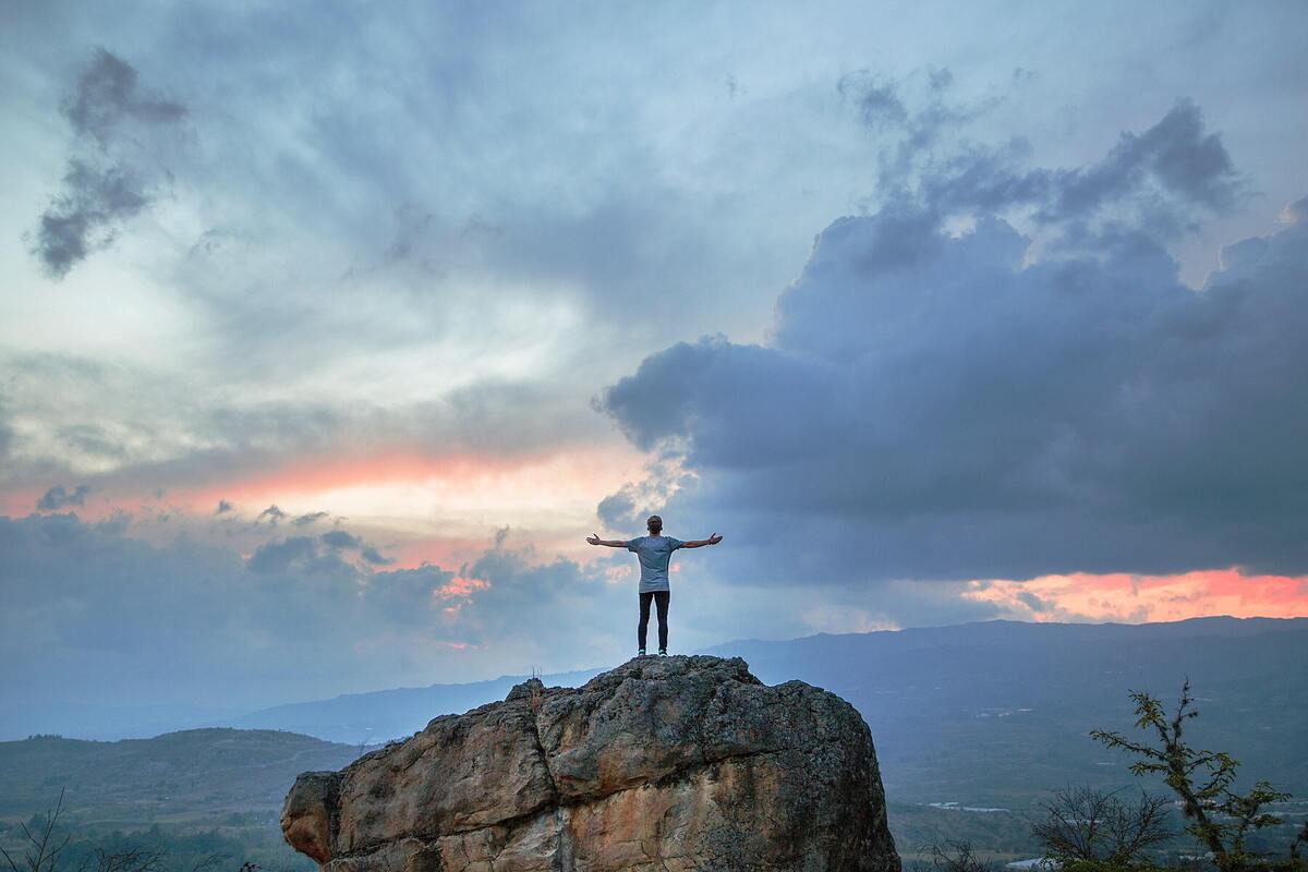 Homem de braços abertos em cima de uma pedra.