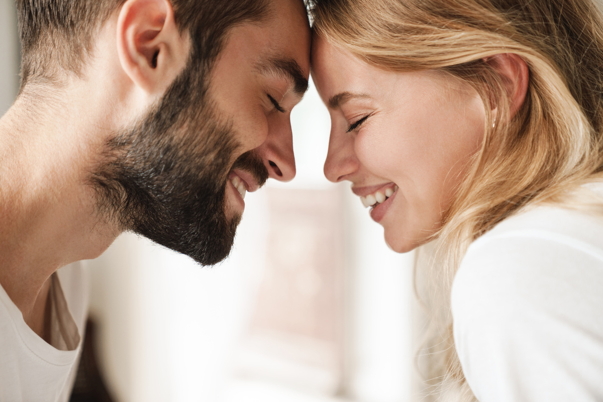 Marido e esposa com as testas juntas, ambos de olhos fechados enquanto sorriem.