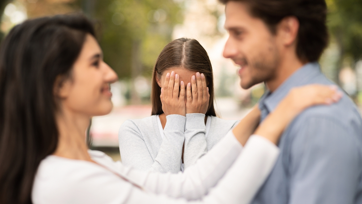 Mulher com as mãos no rosto para não ver casal.