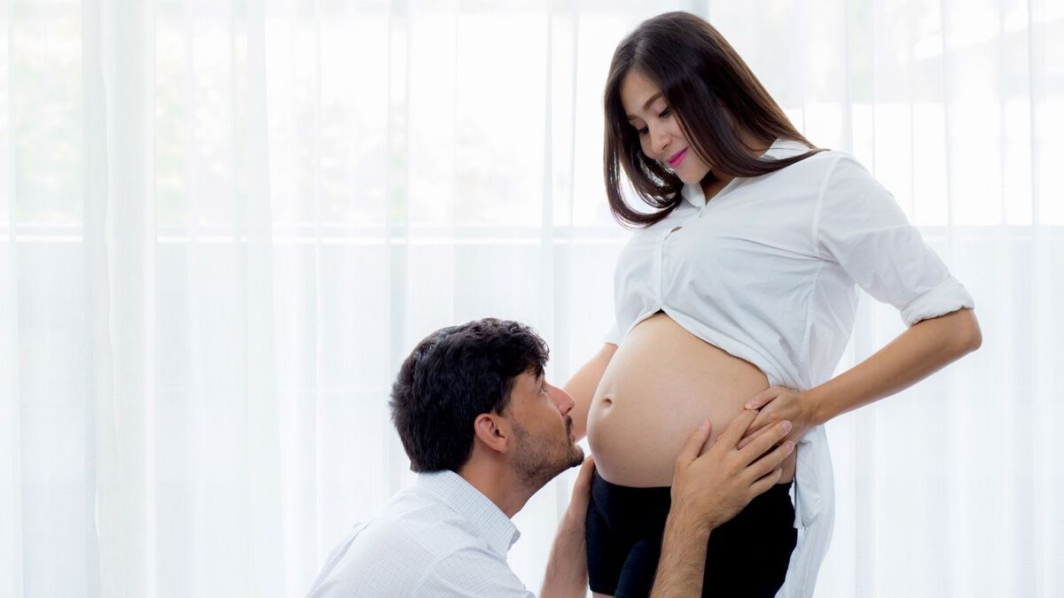 Marido beijando a barriga da esposa grávida.