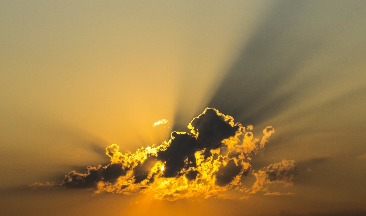 Céu amarelado com luzes do sol saindo por trás de nuvem escura