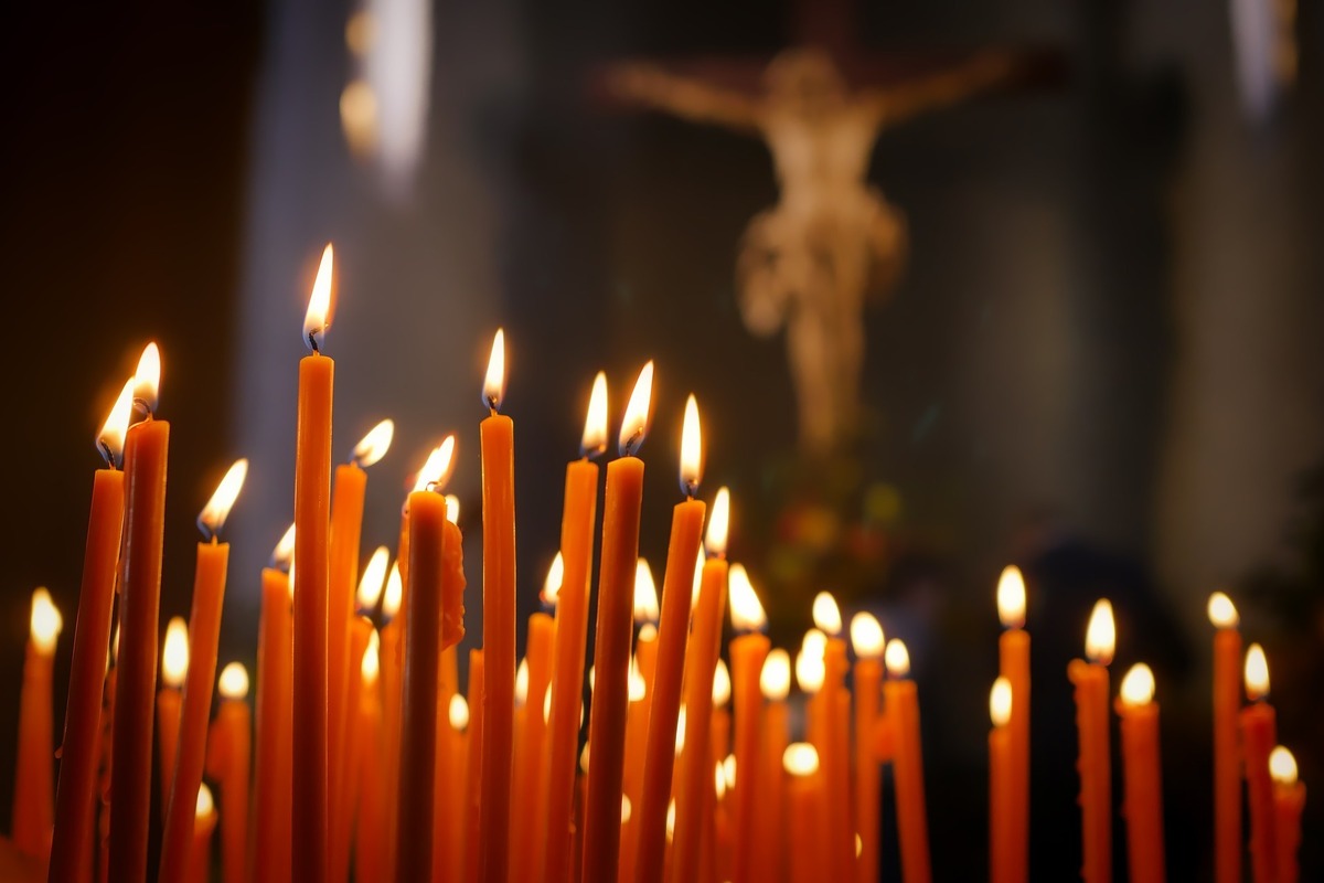 Velas longas acesas em primeiro plano. Em segundo plano, a imagem de Jesus crucificado pendurada em altar.