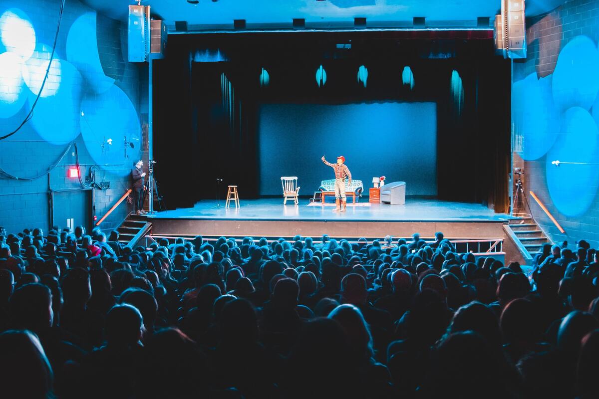 Ator em cima de um palco, plateia cheia. 