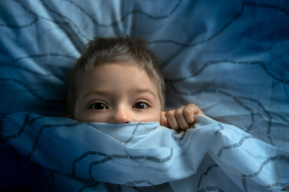 Menino assustado deitado na cama.