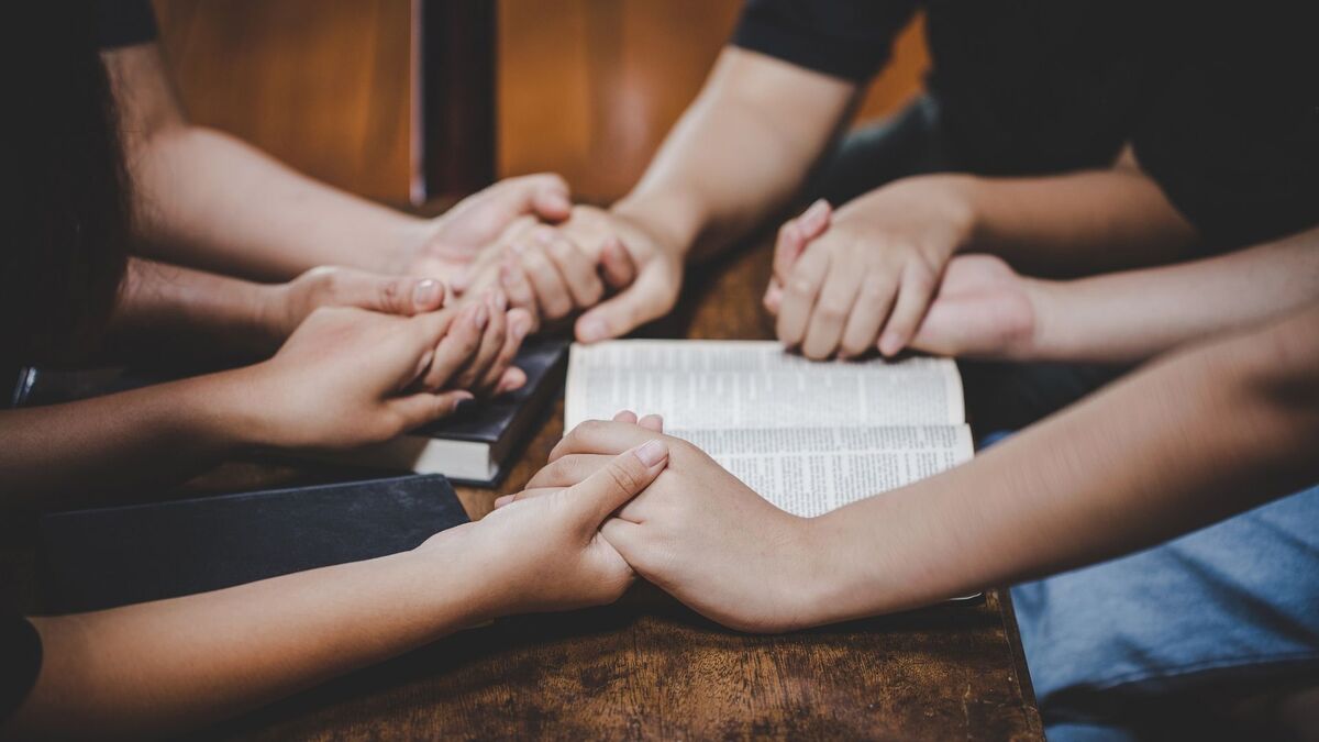 Pessoas de mãos dadas em volta de uma bíblia.