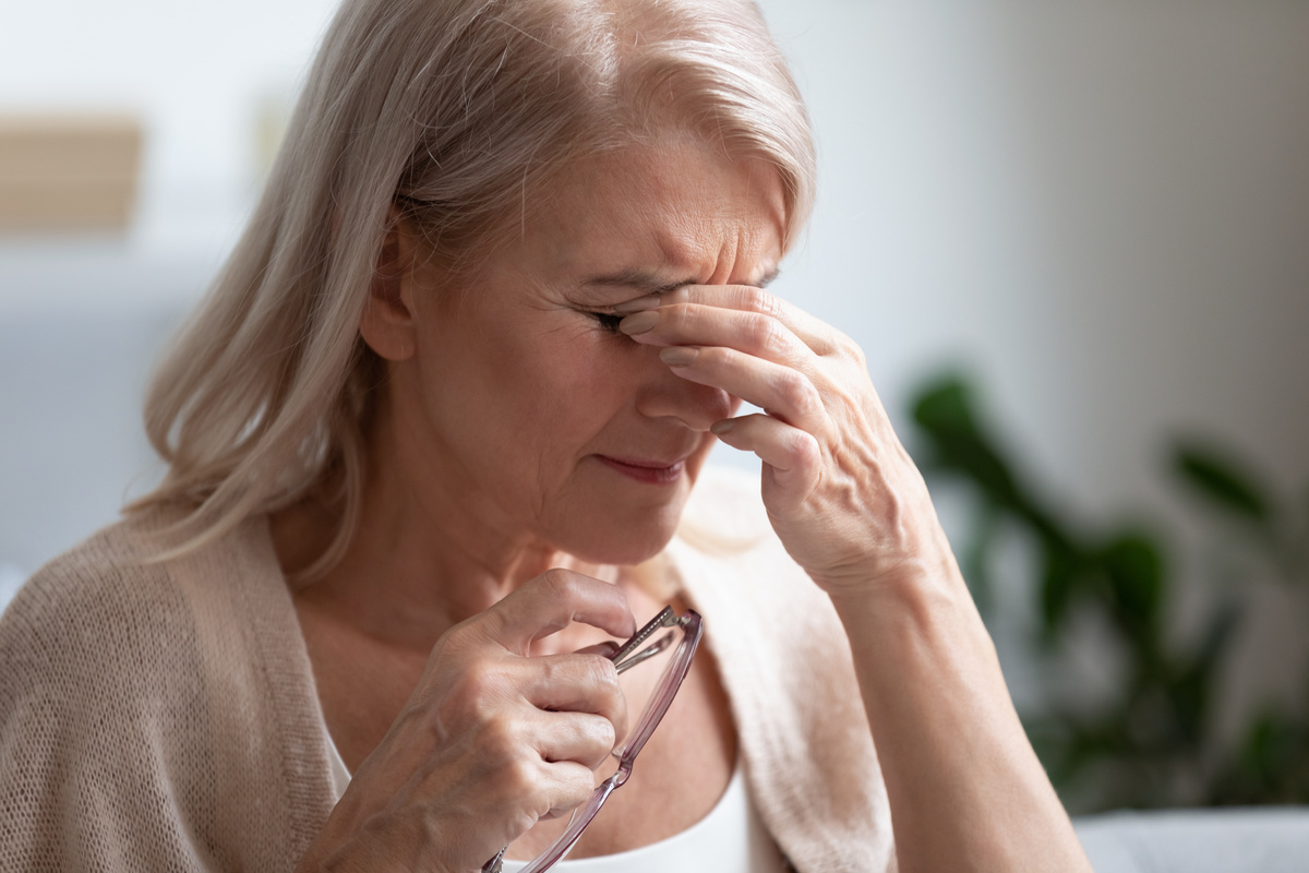 Senhora com óculos na mão e com a outra nos olhos