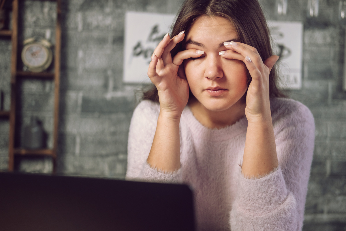 Mulher na frente do computador com as mãos nos olhos