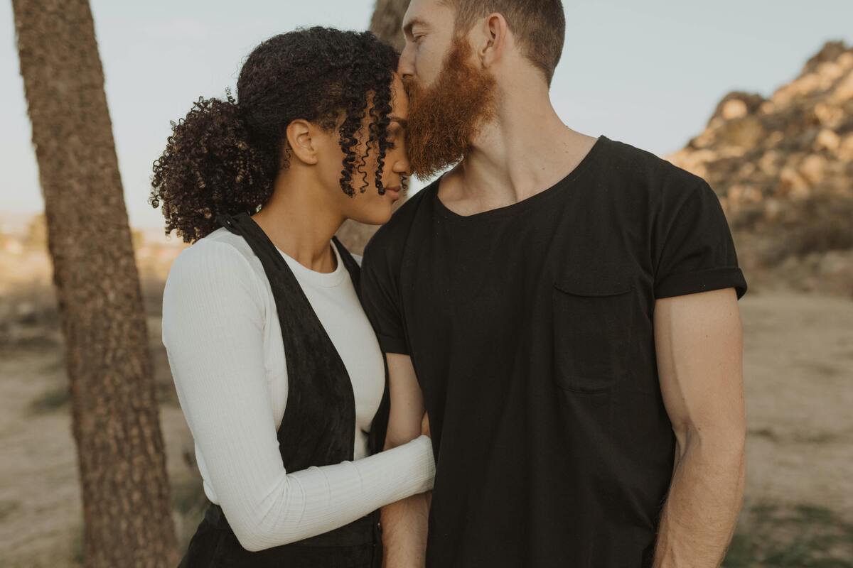 Homem beijando a teste de uma mulher enquanto ela o abraça.