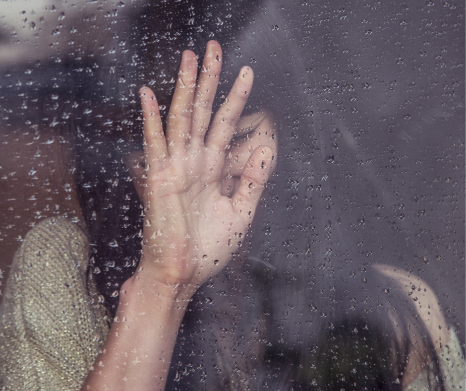 Mulher triste com uma das mãos sob o vidro molhado