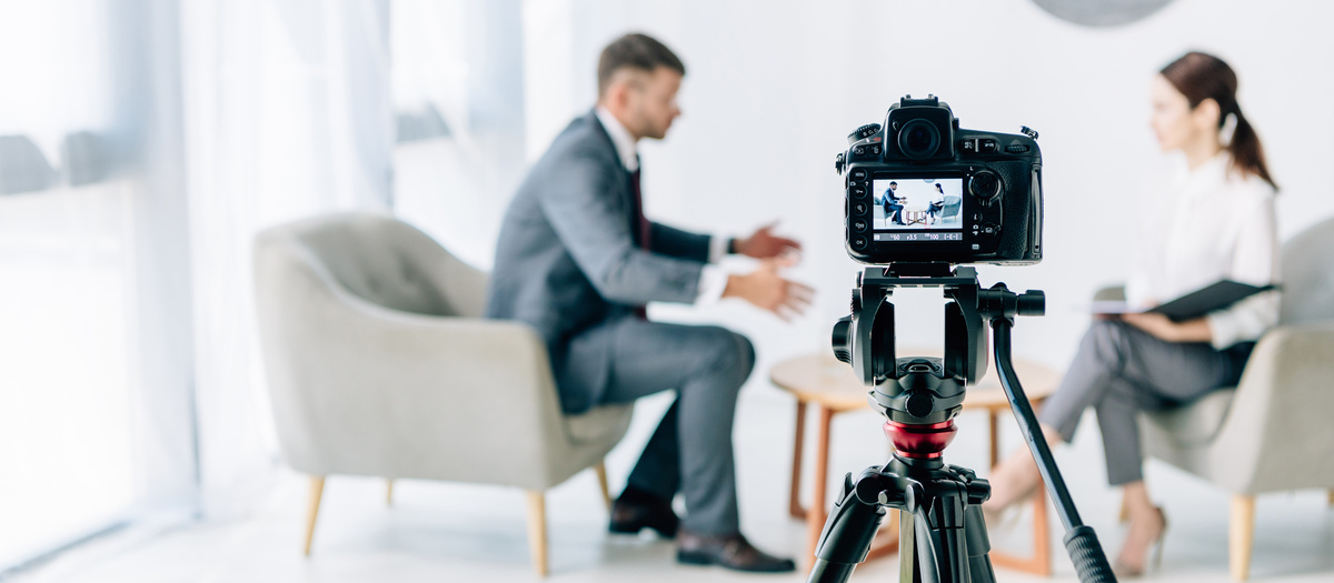 Câmera gravando homem sendo entrevistado por jornalista