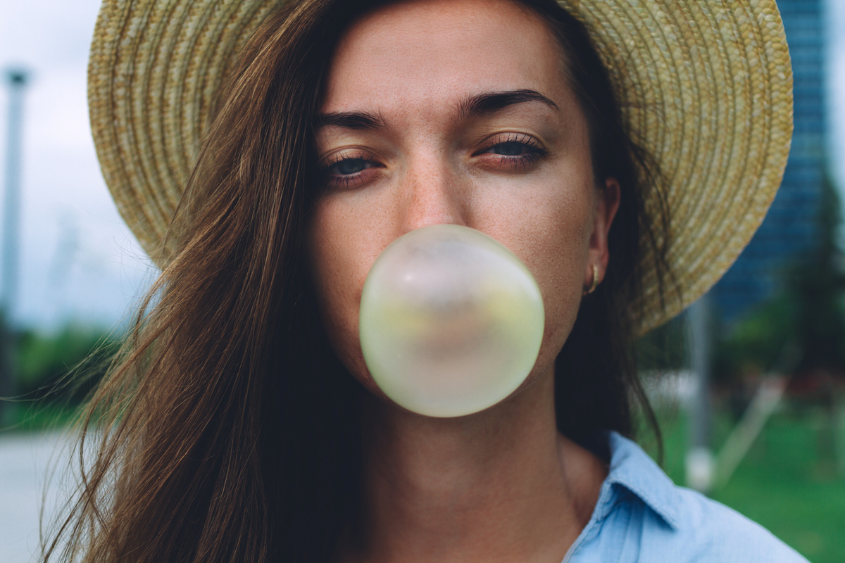 Mulher com chapéu fazendo bola de chiclete