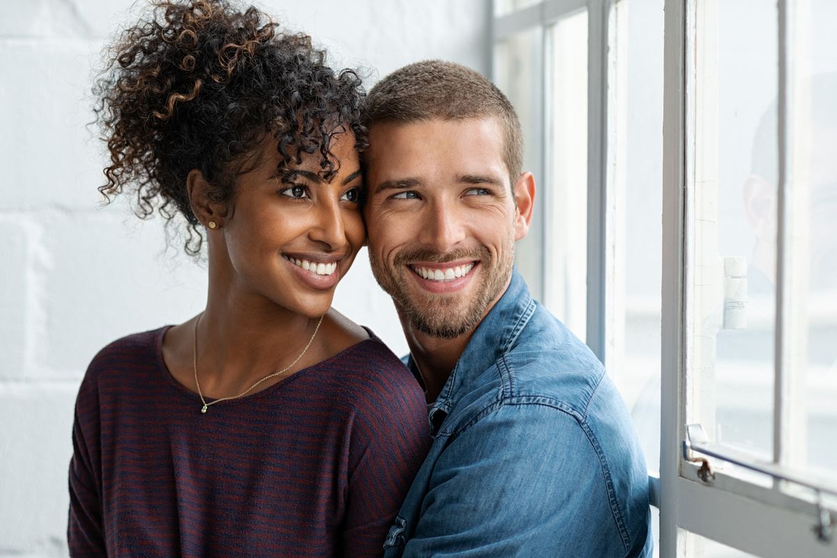 Casal abraçado sorrindo e olhando pela janela