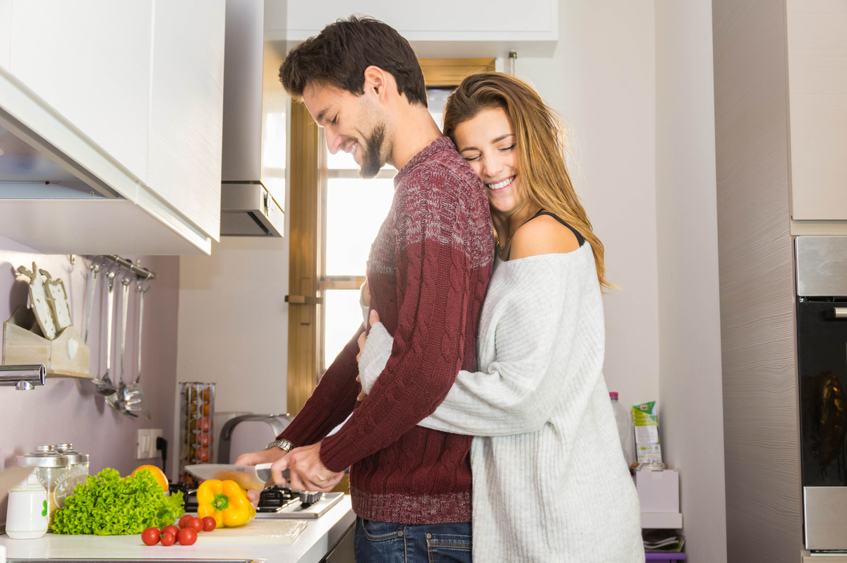 Mulher abraçando homem que está cozinhando