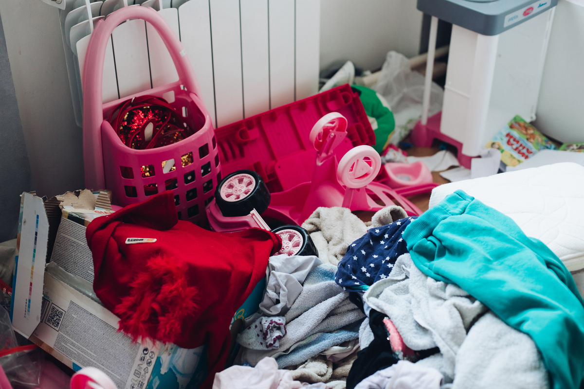 Quarto de casa bagunçada, com diversos objetos empilhados, como brinquedos e roupas. 