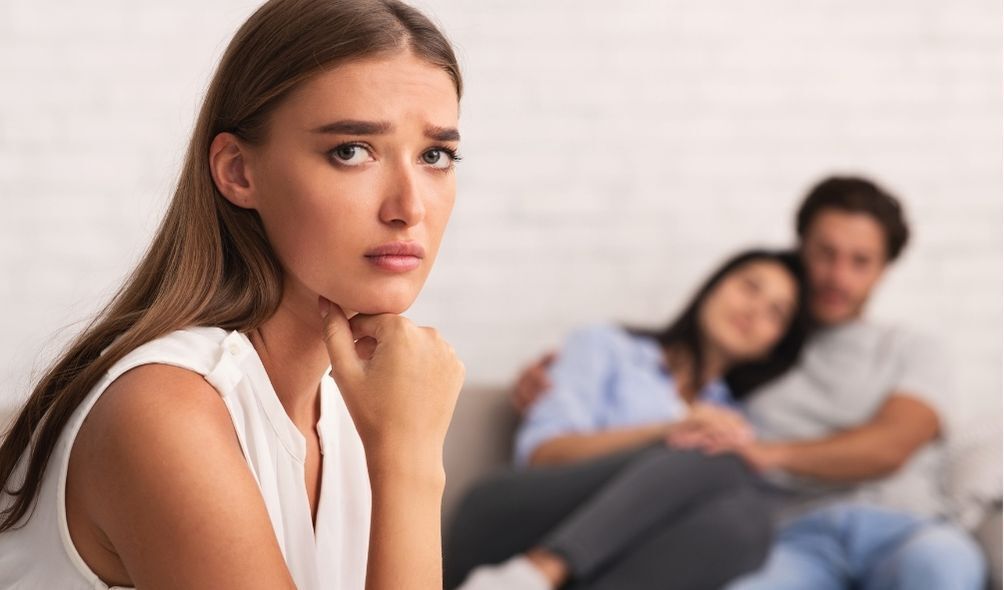 Mulher olhando triste para câmera e casal ao fundoo